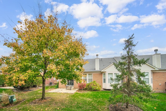 back of property with a patio area, a shingled roof, brick siding, and a yard