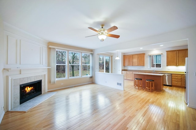 unfurnished living room with visible vents, a tiled fireplace, ceiling fan, a sink, and light wood-type flooring