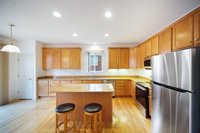 kitchen featuring a breakfast bar area, stainless steel appliances, a kitchen island, a sink, and light wood-style floors