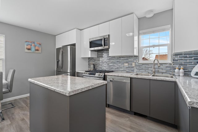 kitchen featuring light wood-style flooring, a kitchen island, a sink, appliances with stainless steel finishes, and tasteful backsplash