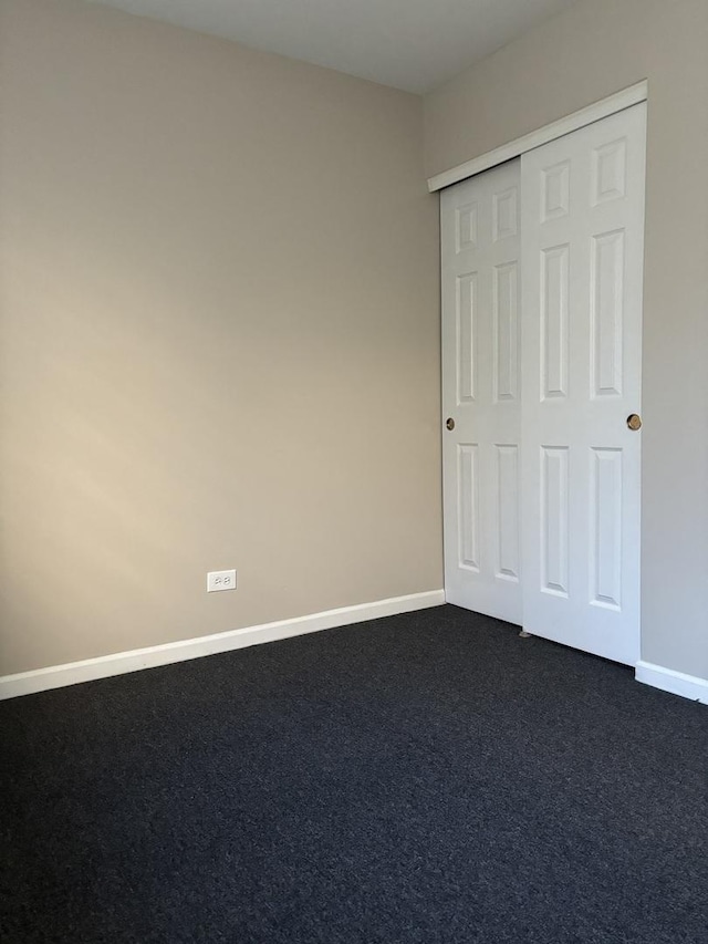 unfurnished bedroom with dark colored carpet, a closet, and baseboards