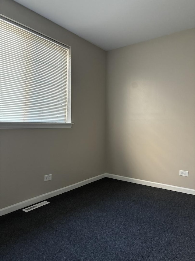 spare room with baseboards, visible vents, and dark carpet