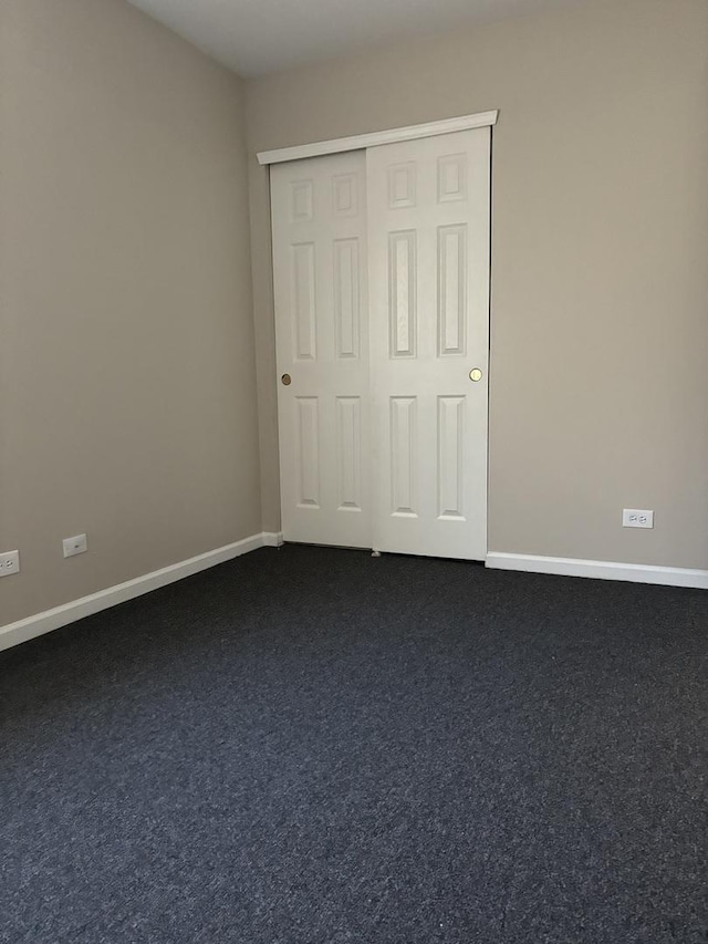 unfurnished bedroom featuring baseboards, dark colored carpet, and a closet