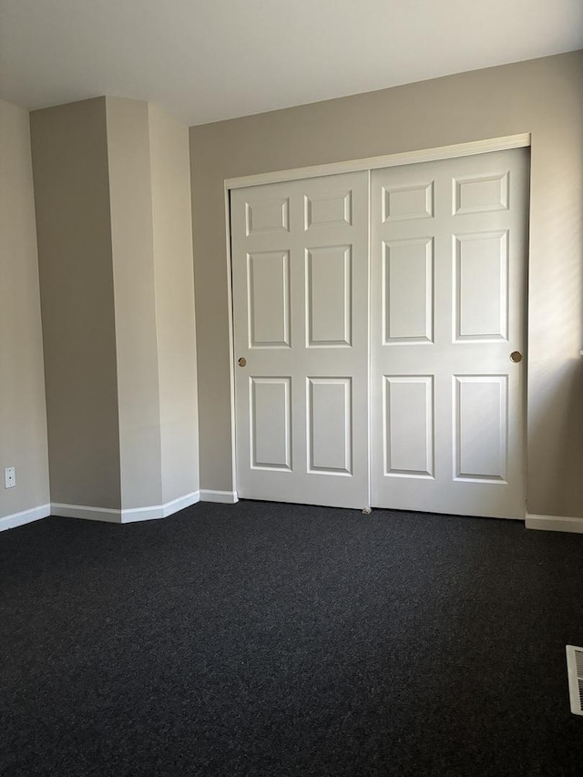 unfurnished bedroom with a closet, dark carpet, visible vents, and baseboards