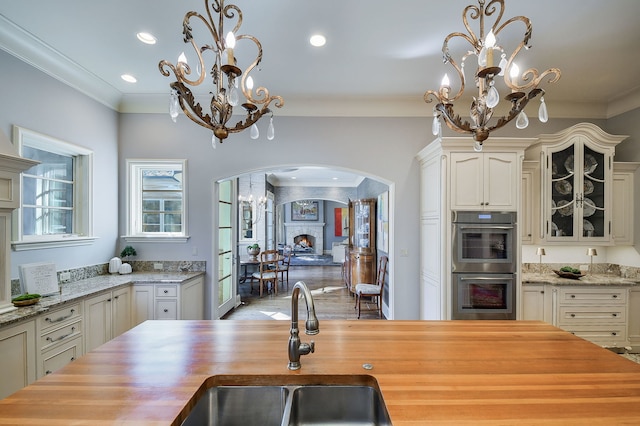 kitchen with a sink, stainless steel double oven, an inviting chandelier, and butcher block counters