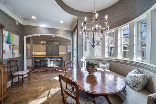 dining room featuring visible vents, crown molding, arched walkways, a notable chandelier, and wood-type flooring