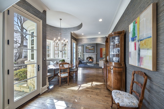 entryway featuring a notable chandelier, a warm lit fireplace, recessed lighting, wood-type flooring, and crown molding