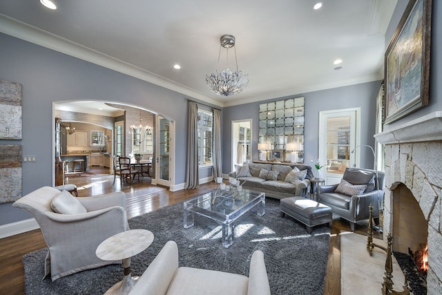 living room featuring crown molding, a notable chandelier, a fireplace, and arched walkways