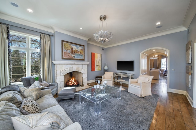 living room featuring dark wood-type flooring, arched walkways, a stone fireplace, an inviting chandelier, and baseboards