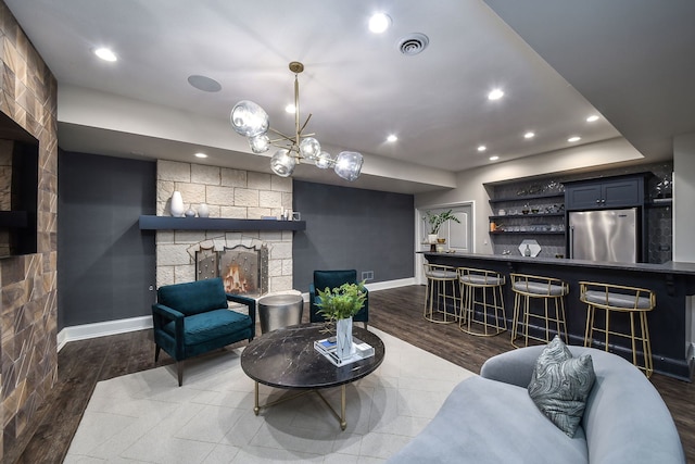 living room with visible vents, wood finished floors, recessed lighting, a stone fireplace, and baseboards