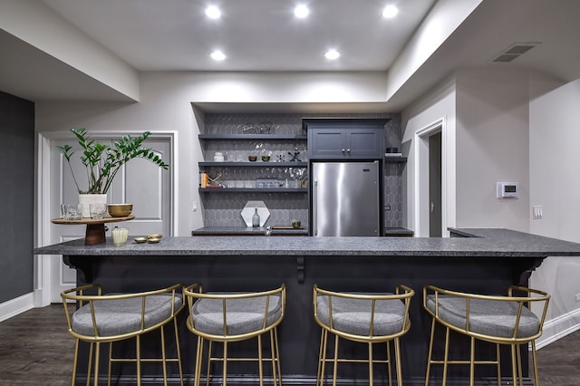 bar with visible vents, dark wood-style floors, high end refrigerator, and a dry bar