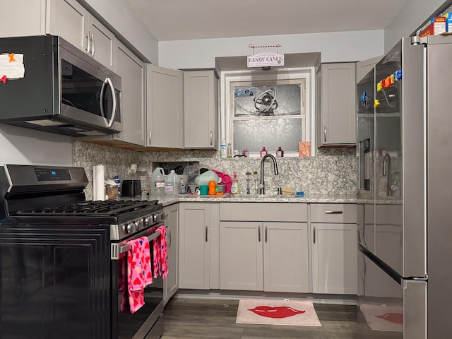 kitchen with gray cabinets, dark wood-style flooring, a sink, decorative backsplash, and appliances with stainless steel finishes