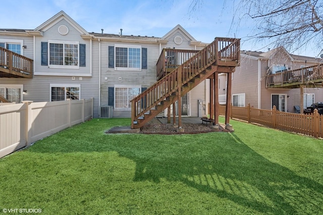 back of property with a lawn, a wooden deck, stairs, and a fenced backyard