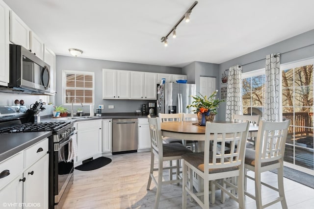 kitchen featuring dark countertops, appliances with stainless steel finishes, light wood-style floors, white cabinetry, and a sink