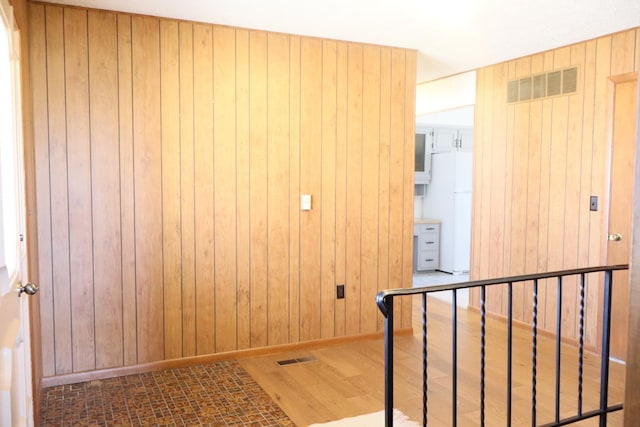 hall with wooden walls, wood finished floors, visible vents, and baseboards