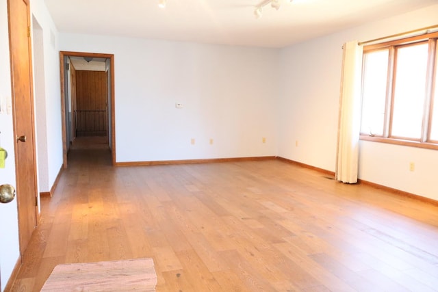 empty room with track lighting, light wood-type flooring, and baseboards