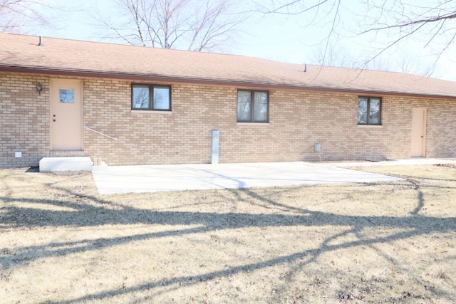 rear view of house featuring a patio, brick siding, entry steps, and a shingled roof