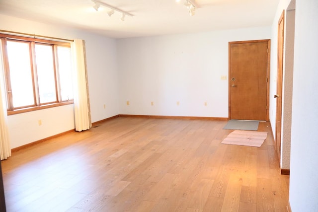 unfurnished room featuring track lighting, baseboards, and light wood-style floors