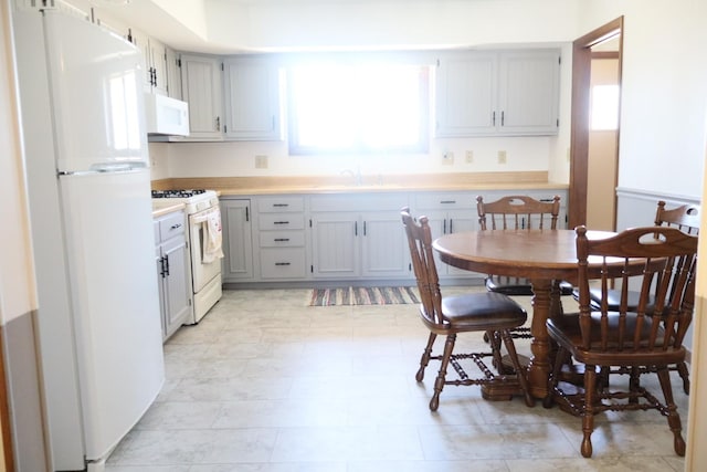 kitchen with a sink, white appliances, gray cabinetry, and light countertops