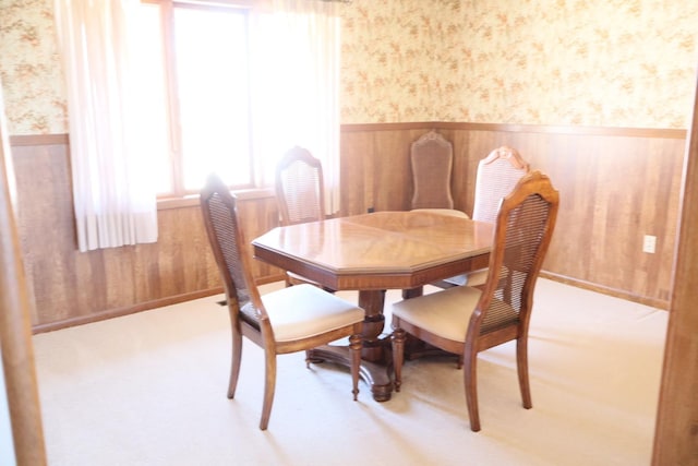 dining space featuring wallpapered walls, wooden walls, carpet flooring, and a wainscoted wall