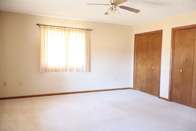 unfurnished bedroom with baseboards, carpet, multiple closets, and a ceiling fan