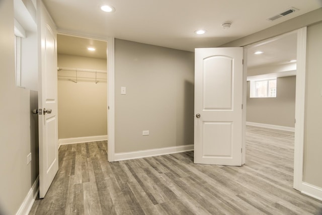 interior space with light wood finished floors, visible vents, a walk in closet, and baseboards