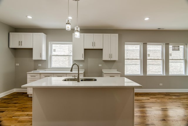 kitchen with baseboards, wood finished floors, hanging light fixtures, white cabinets, and a sink