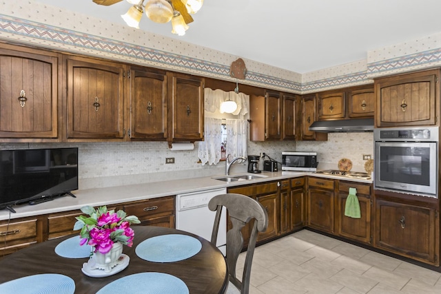 kitchen with wallpapered walls, under cabinet range hood, light countertops, appliances with stainless steel finishes, and a sink