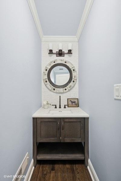 bathroom with baseboards, wood finished floors, ornamental molding, and vanity