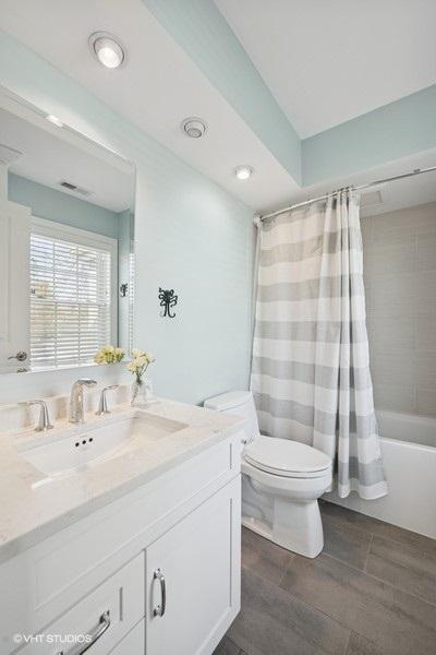 full bath featuring visible vents, shower / bath combination with curtain, toilet, and vanity