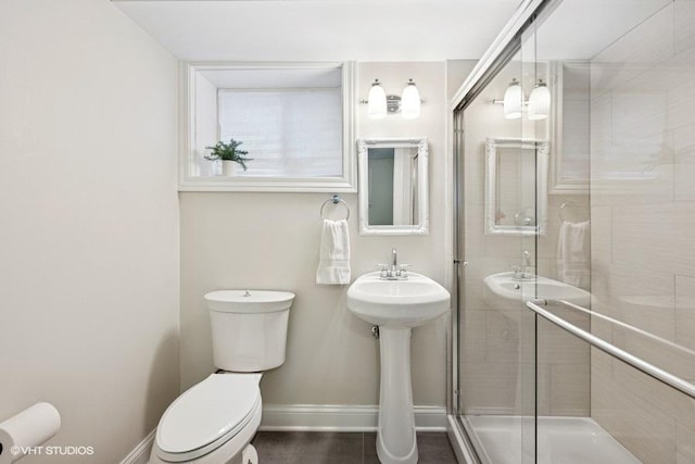 bathroom with a sink, baseboards, toilet, and a stall shower