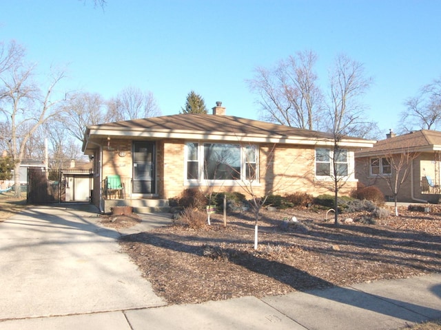 ranch-style home with driveway, brick siding, and a chimney