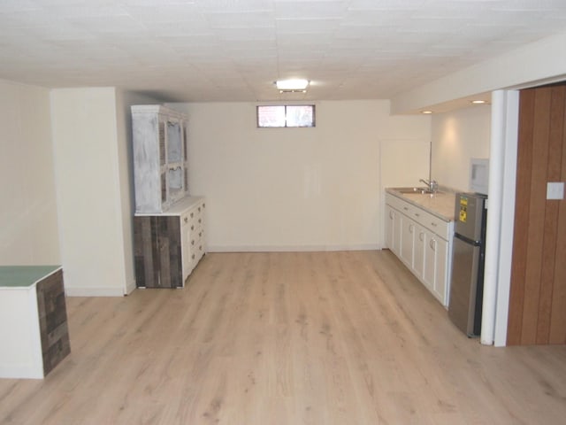 kitchen featuring light wood finished floors, white microwave, freestanding refrigerator, white cabinets, and a sink