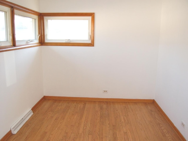 empty room with light wood finished floors, visible vents, and baseboards