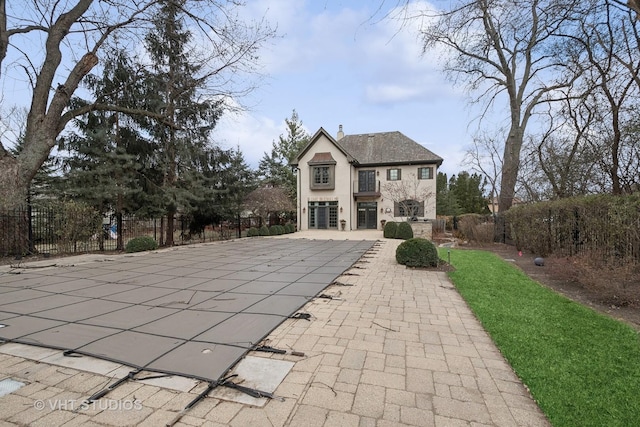 rear view of house featuring a chimney, stucco siding, a patio area, fence, and stone siding