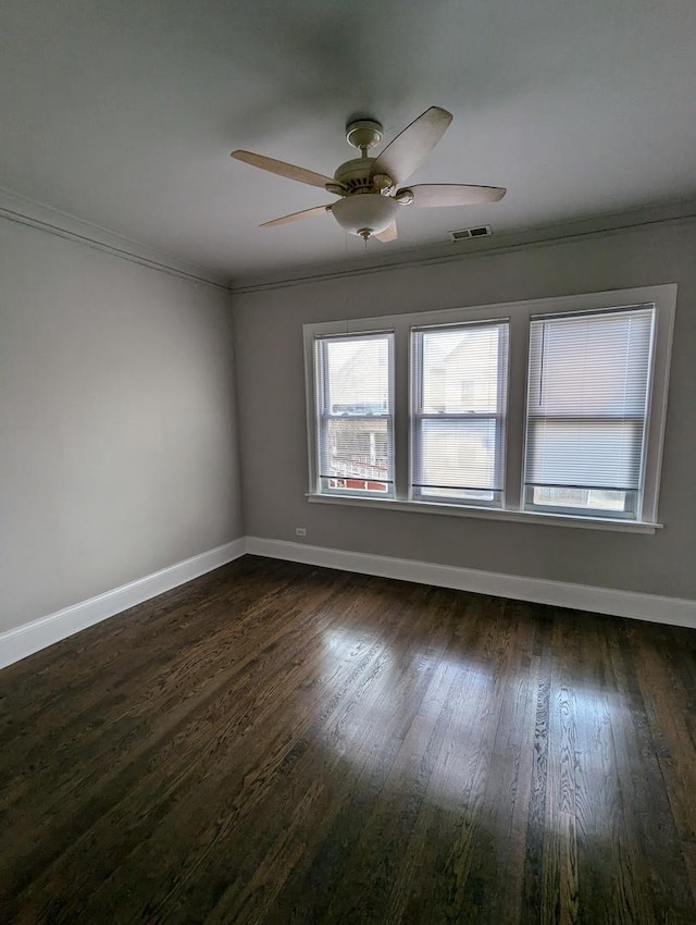 empty room featuring a ceiling fan, baseboards, visible vents, dark wood finished floors, and crown molding