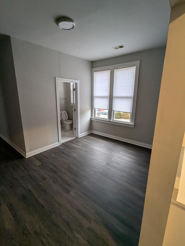 unfurnished bedroom featuring visible vents, baseboards, ensuite bath, and dark wood finished floors