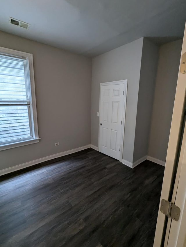 spare room featuring dark wood-style floors, visible vents, and baseboards