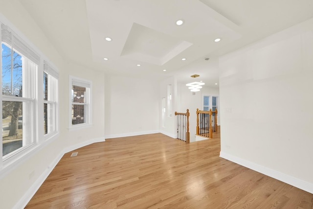 empty room featuring a tray ceiling, light wood-style flooring, recessed lighting, and baseboards