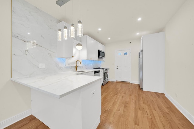 kitchen featuring light wood finished floors, a peninsula, a sink, white cabinetry, and backsplash