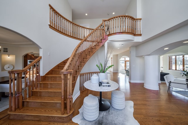 staircase featuring baseboards, arched walkways, a high ceiling, and wood finished floors