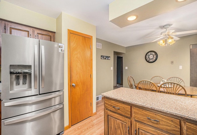 kitchen featuring visible vents, brown cabinets, stainless steel fridge with ice dispenser, and light stone countertops