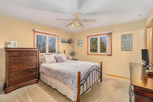 bedroom featuring multiple windows, a ceiling fan, baseboards, and light carpet