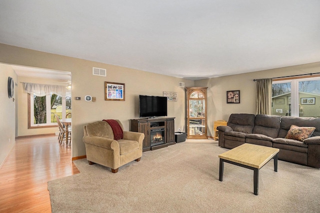 living room with light wood finished floors, visible vents, baseboards, and a lit fireplace