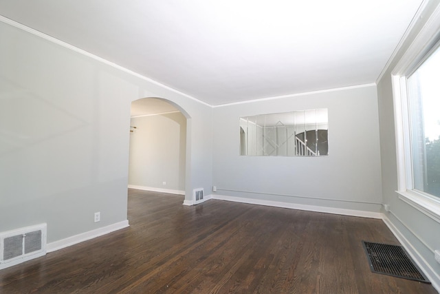 spare room featuring visible vents, arched walkways, and dark wood-style floors