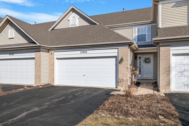 townhome / multi-family property with aphalt driveway, a garage, brick siding, and a shingled roof