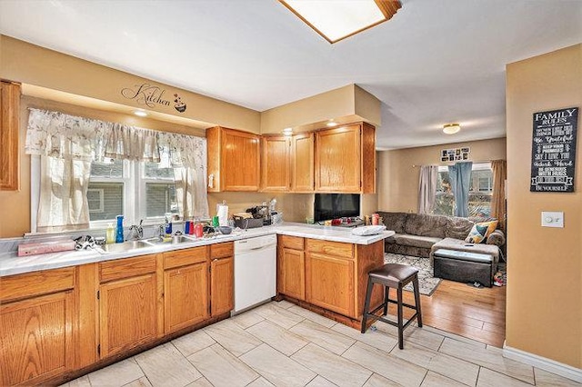 kitchen with open floor plan, dishwasher, a breakfast bar, light countertops, and a peninsula