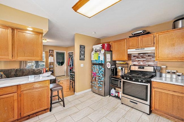 kitchen with under cabinet range hood, stainless steel appliances, light countertops, and baseboards