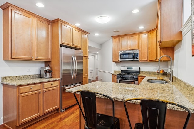 kitchen featuring light stone counters, light wood-style flooring, a peninsula, stainless steel appliances, and a sink