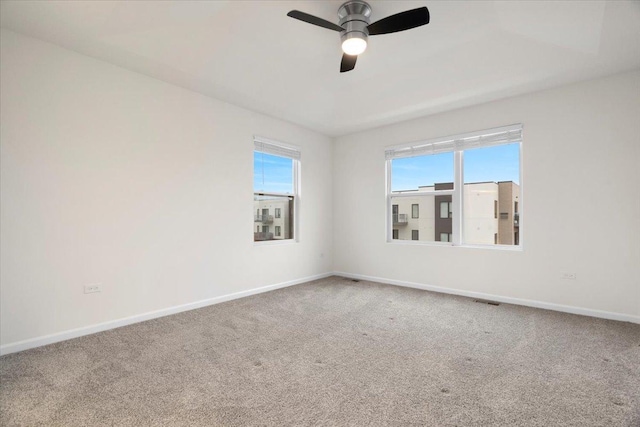 carpeted spare room with visible vents, baseboards, and ceiling fan